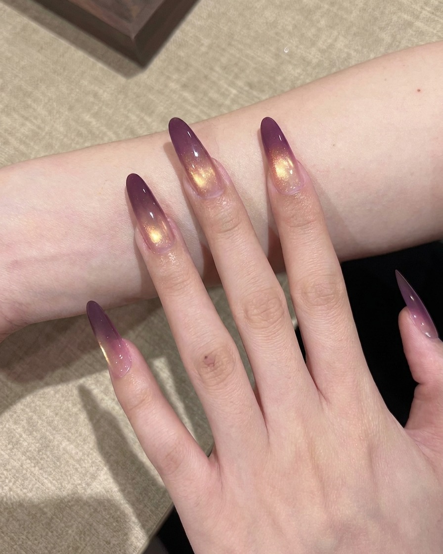 Eine Hand mit violett-goldenen Verlauf-Nägeln in einer professionellen UV-Nagellampe beim Aushärten.