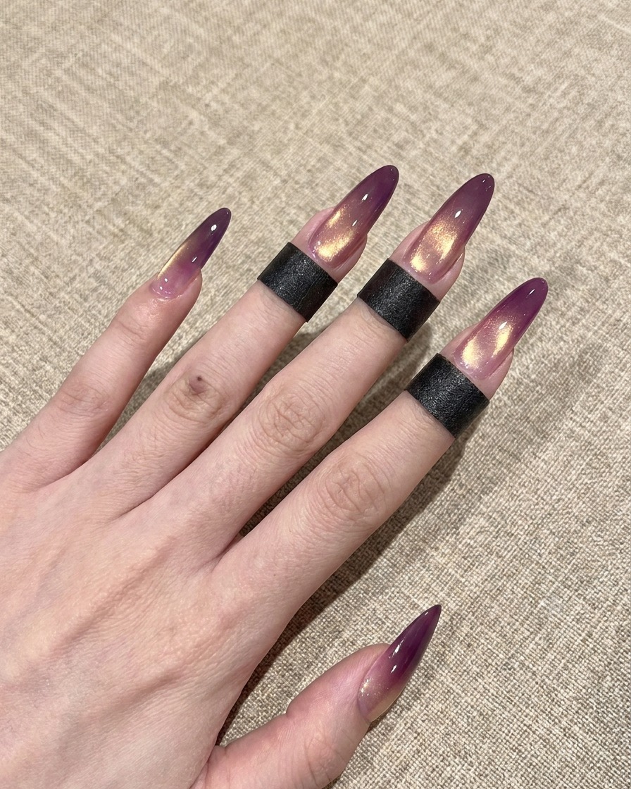Ein Pinsel trägt einen glänzenden klaren Überlack auf einen violetten und goldenen Cat-Eye-Nagel auf.