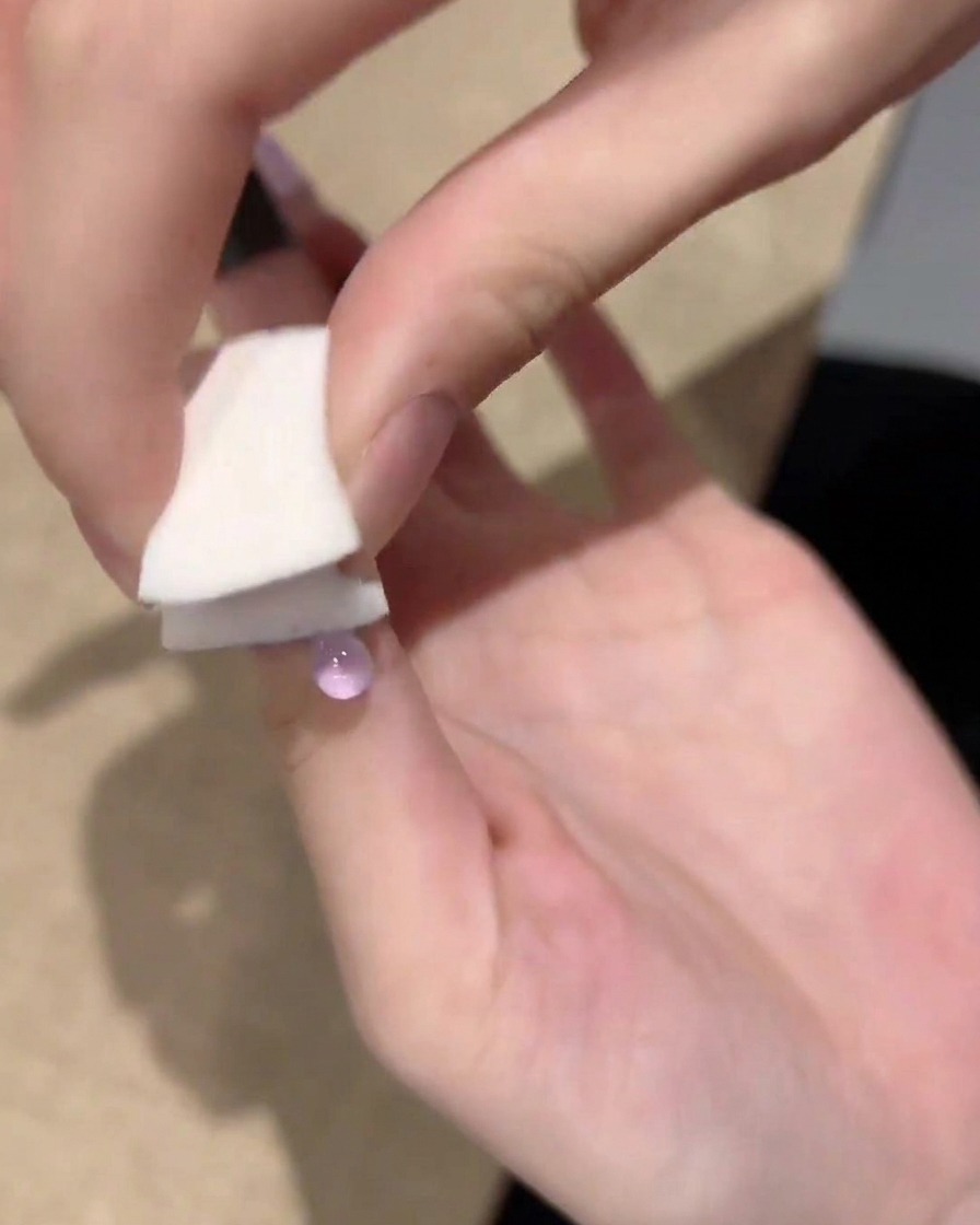 Eine Hand benutzt einen kleinen weißen Schwamm, um lila Gelpolitur von der Nagelspitze zur Mitte hin abzutupfen und zu verblenden.