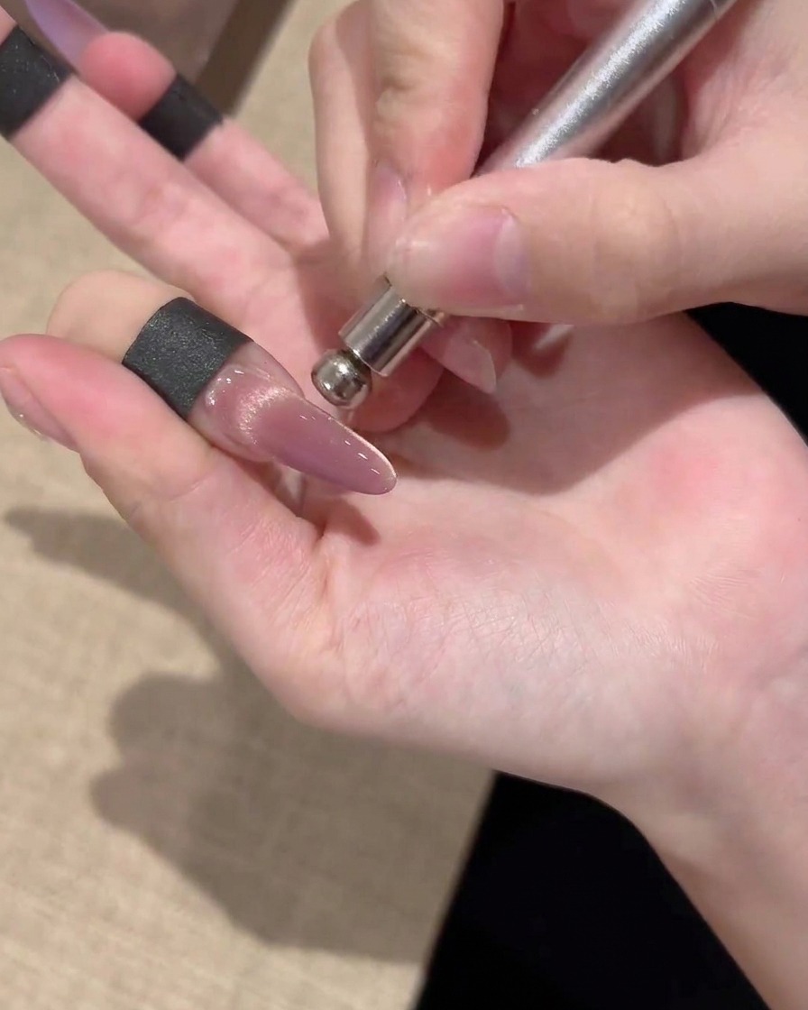 Ein zylindrischer Magnet, der neben einem Nagel gehalten wird, um goldene magnetische Partikel zu einem hellen Mittelband zu führen.
