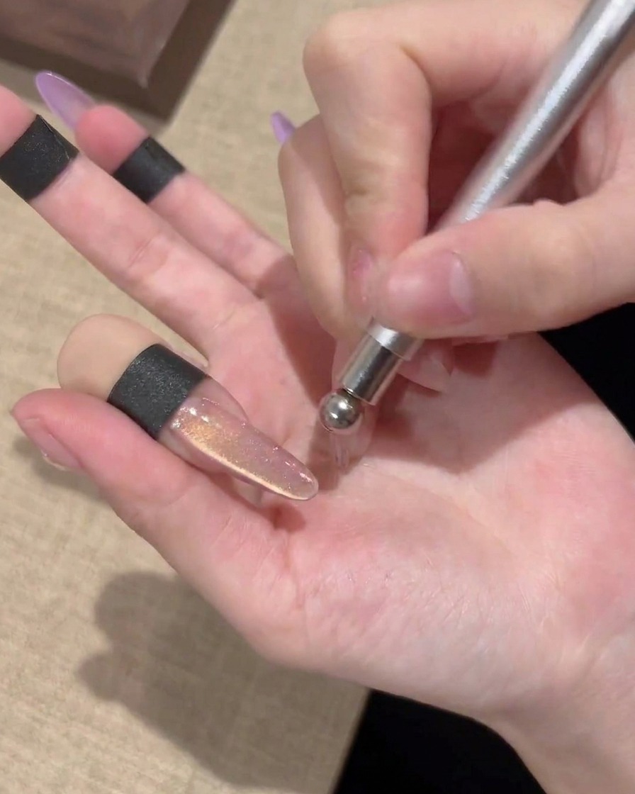 Die Kugelseite eines Magnetstabes erzeugt ein kreisförmiges Wirbelmuster auf einem Cat-Eye-Gel-Nagel.