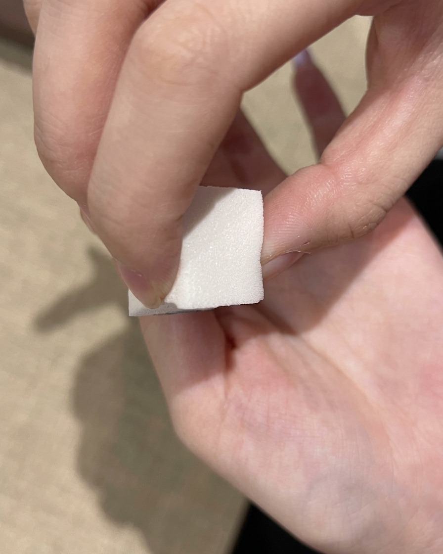 Ein weißer Make-up-Schwamm tupft tief-lilafarbenes Gel auf den freien Rand eines Nagels.