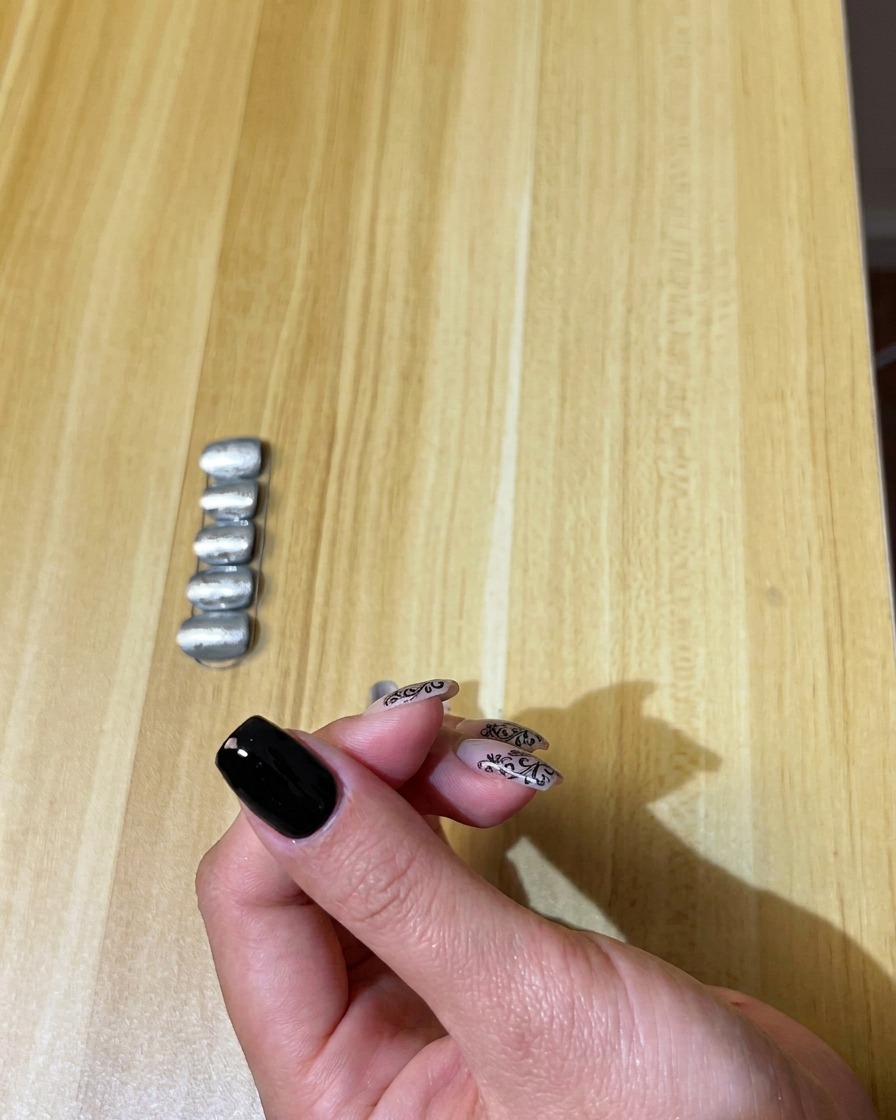 Ein Pinsel trägt eine gleichmäßige Schicht schwarzen Gellacks auf einen Naturnagel auf.