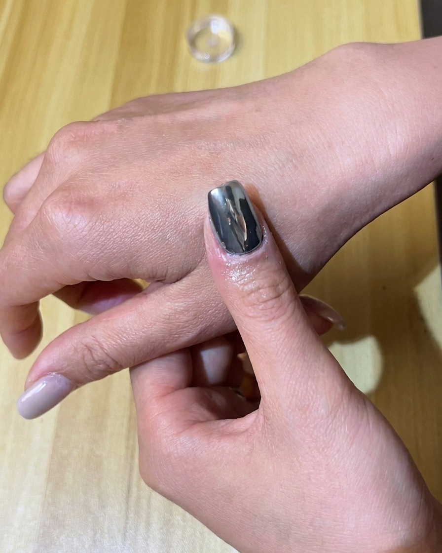 Ein Schwammapplikator reibt silbernes Chrompigment auf einen mit schwarzem Gel lackierten Nagel.