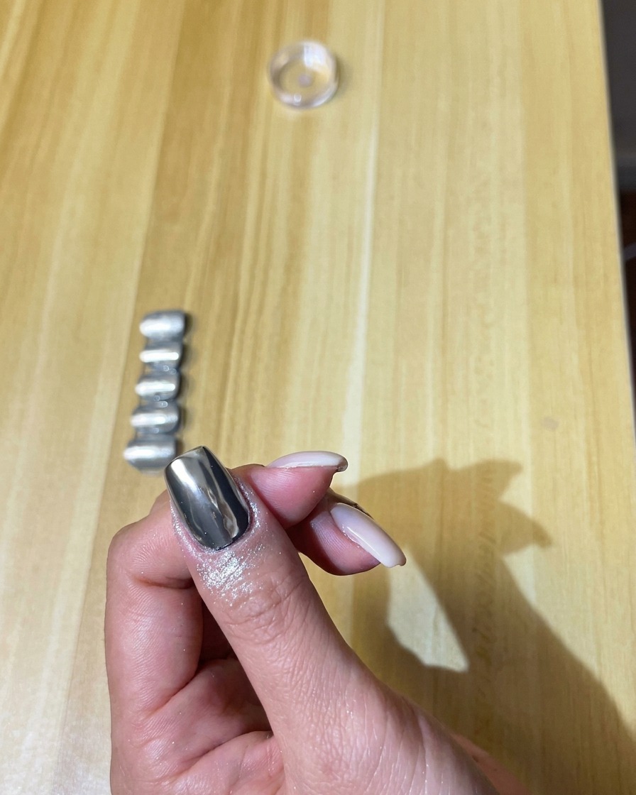 Ein flauschiger Make-up-Pinsel bürstet vorsichtig überschüssiges silbernes Chrom-Puder vom Nagel.