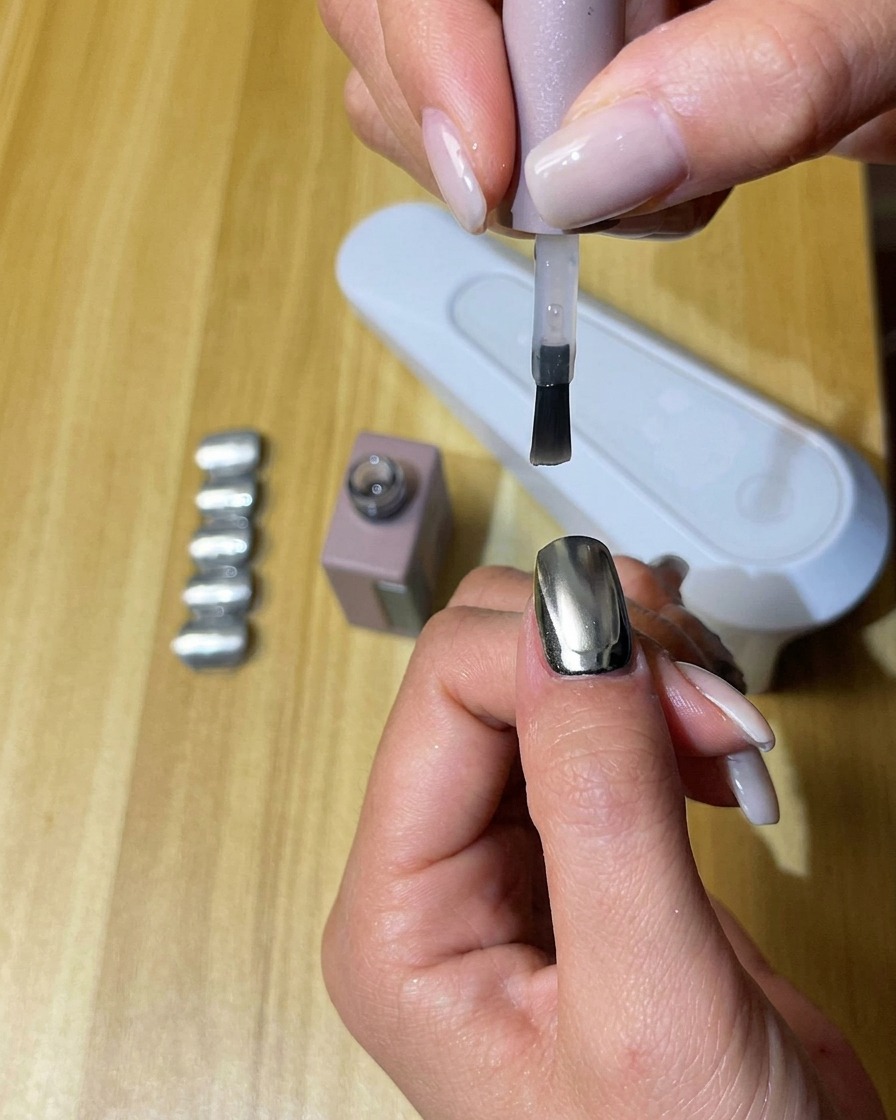 Eine Hand mit Nägeln, die mit mattem Überlack beschichtet sind, härtet in einer UV/LED-Nagellampe aus.