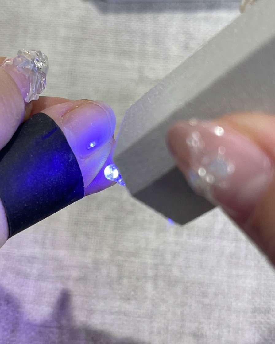 Eine Hand mit dekorierten floralen Nägeln in einer UV-Nagellampe, wobei blaues Licht aus der Maschine die Politur aushärtet.