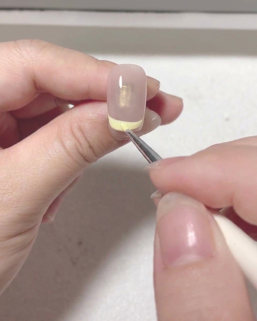 Ein Detailpinsel füllt den roten Farbbereich innerhalb der French-Tip-Linie auf dem Nagel aus.