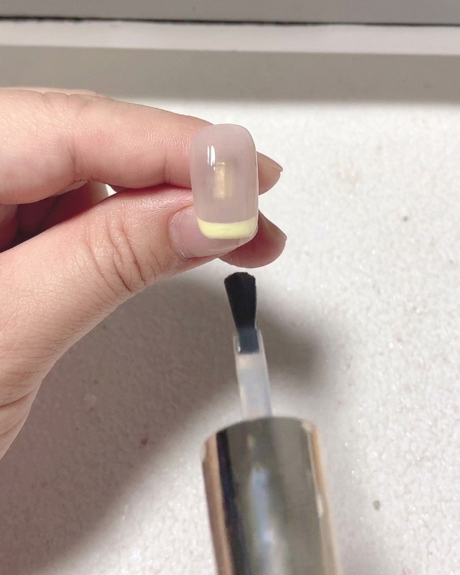 Ein Pinsel trägt ein klares mattes Top Coat über dem rot lackierten French-Tip-Nagel auf.