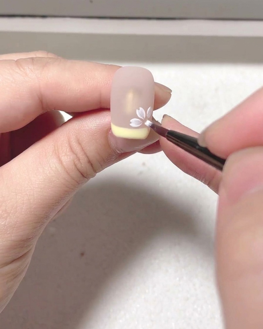 Eine Nahaufnahme zeigt einen Pinsel, der weißes Blooming-Gel aufträgt, um Blütenblattformen auf einer Nude-Oberfläche zu erzeugen.