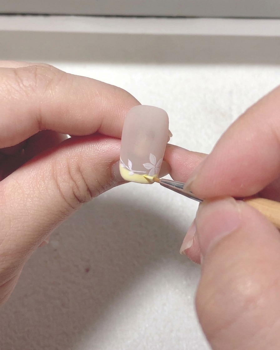 Eine Nahaufnahme eines Liner-Pinsels, der letzte Akzente setzt und Linien auf dem Sakura-Nageldesign verfeinert.