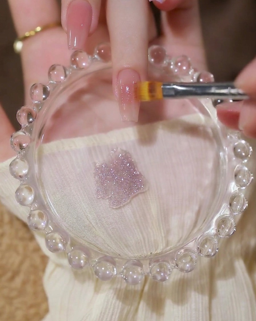 Ein Pinsel trägt eine Schicht glitzerndes Pailletten-Gel über eine Nude-Basis auf.