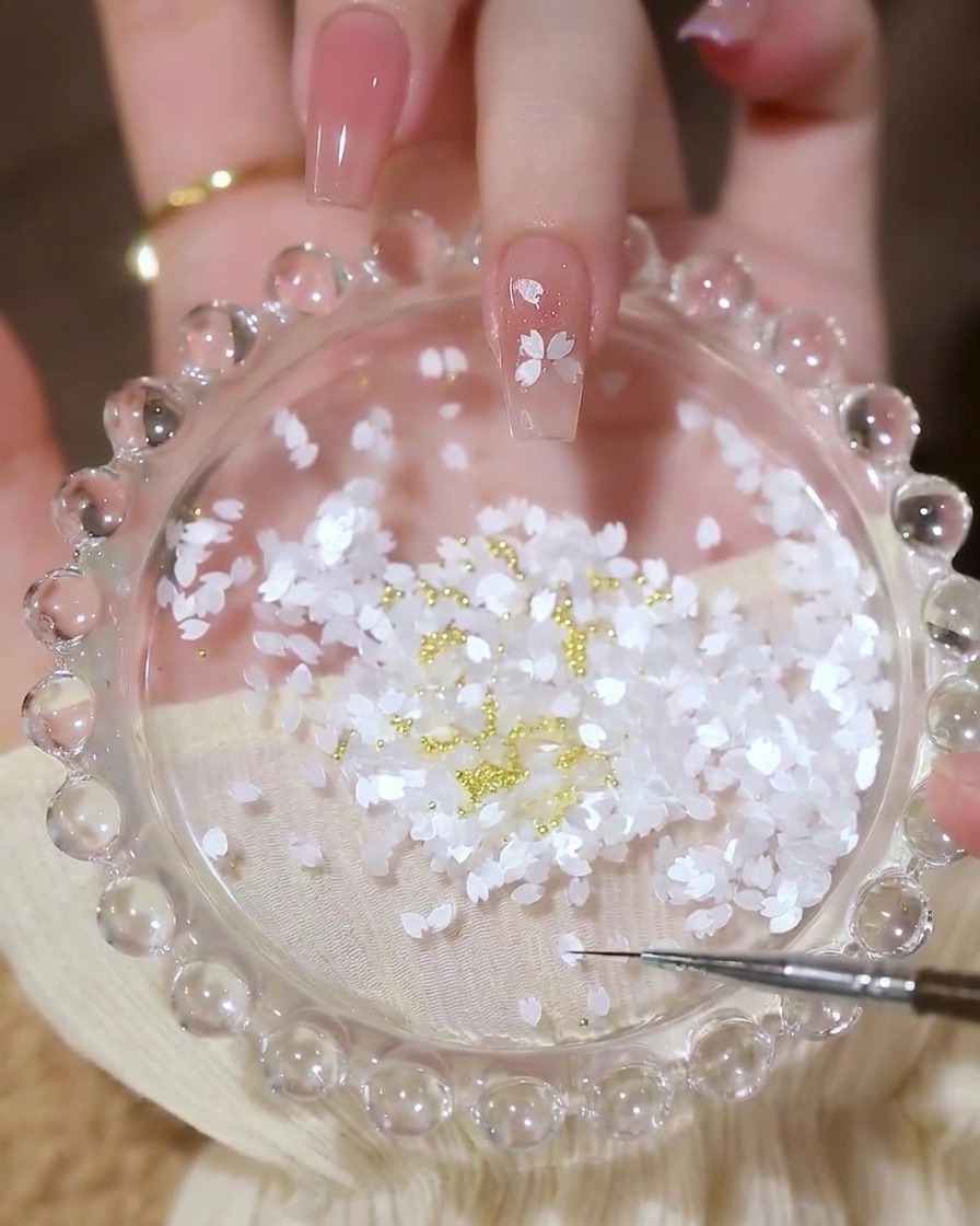 Ein Nagel mit einem fertigen Blumendesign aus Blütenblatt-Pailletten mit einer kleinen goldenen Perle in der Mitte.