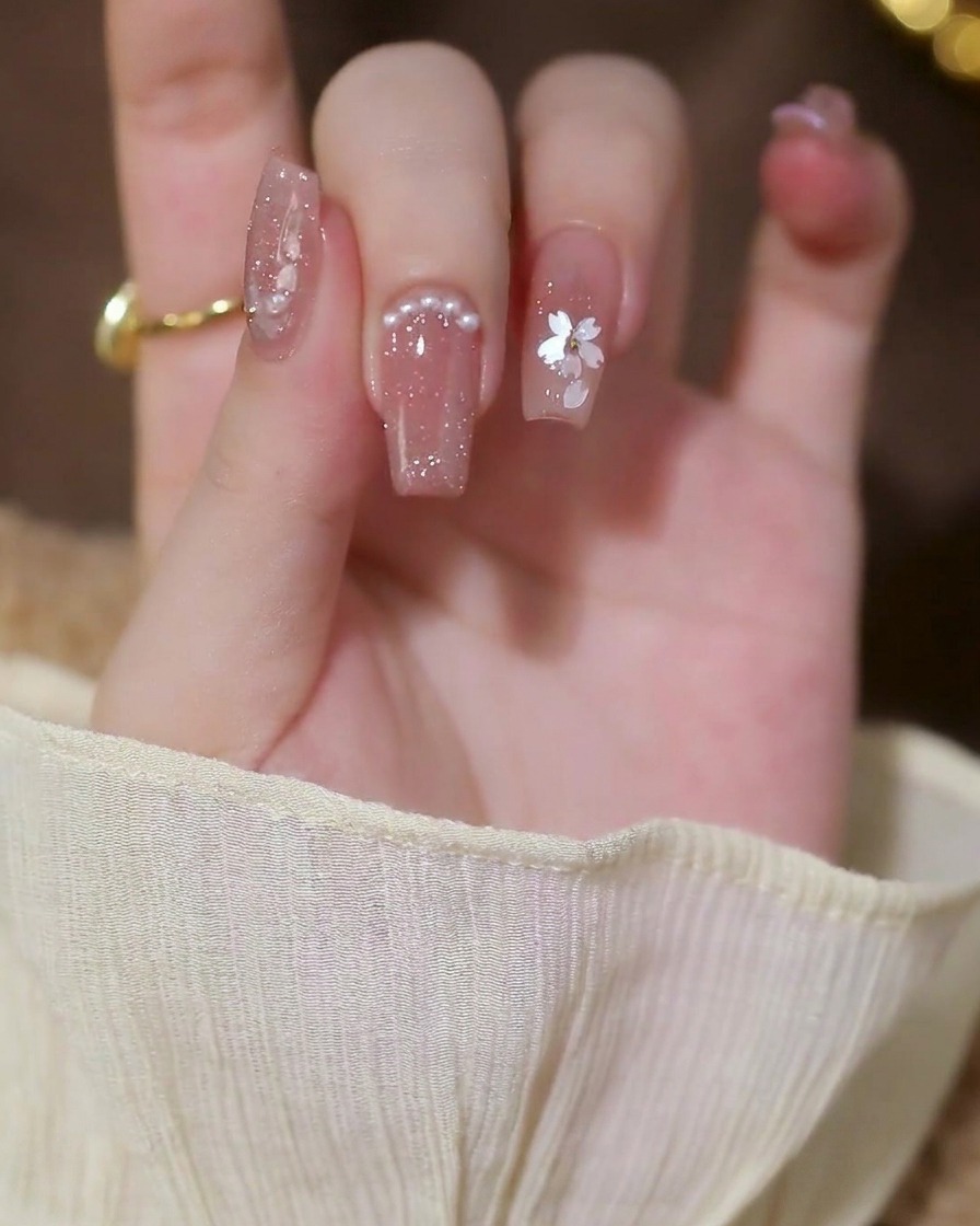Kleine weiße Halbperlen werden in einer Reihe entlang der Nagelhautlinie eines Fingernagels platziert.