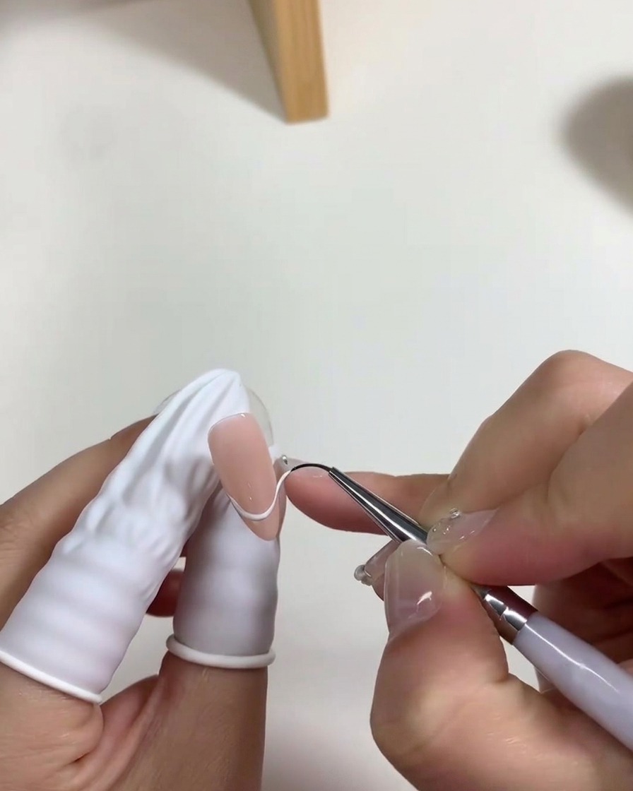 Ein Nagelpinsel trägt eine dünne Schicht milchig-weißes Gel auf das Nagelbett auf.