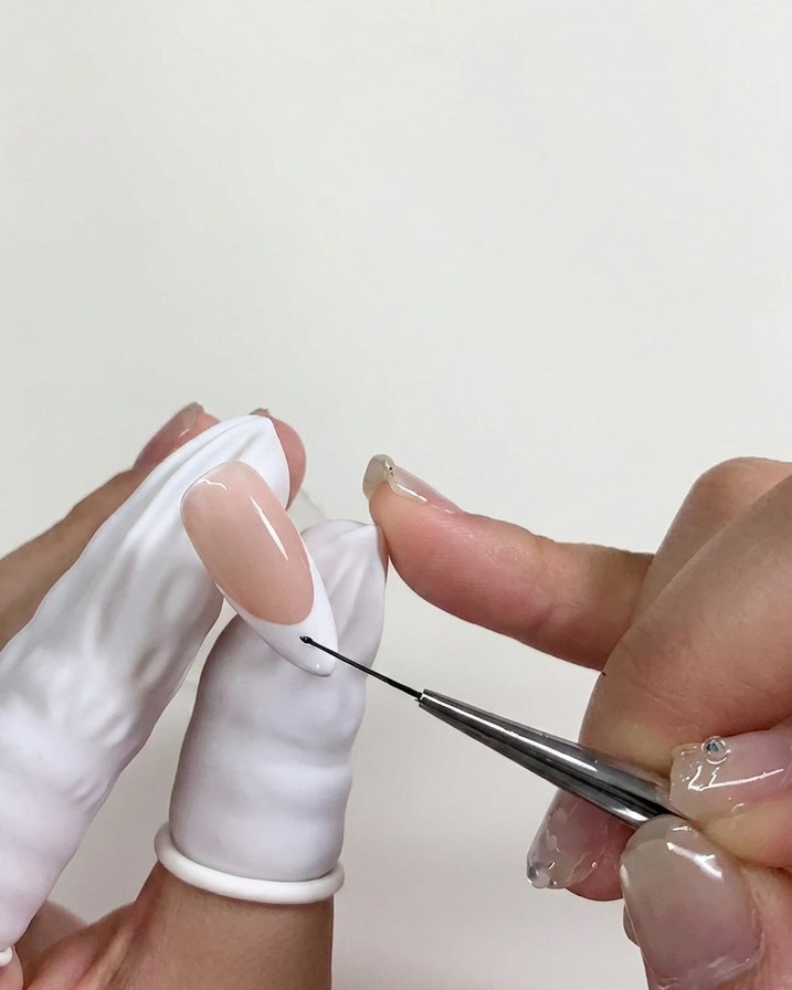 Ein feiner Nail-Art-Pinsel setzt einen winzigen Punkt schwarzes Gel auf die noch feuchte Blooming-Gel-Schicht.