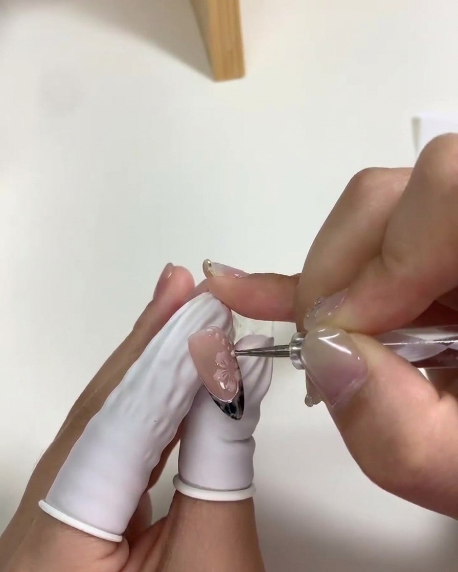 Nahaufnahme eines Dotting-Tools, das kleine weiße Akzentpunkte um die Kirschblüten setzt.