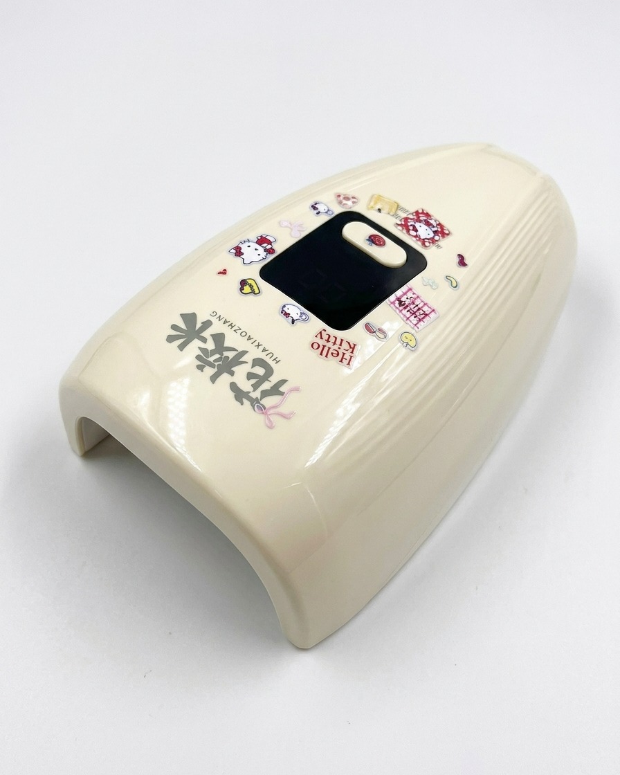 Eine creme-farbene Mini-UV/LED-Lampe mit Hello-Kitty-Stickern steht auf einem weißen Untergrund.