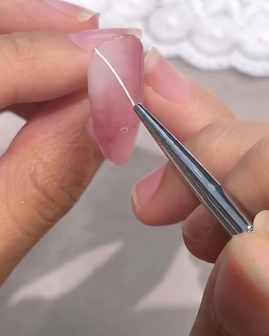 Ein feiner Detailpinsel zeichnet eine dünne, weiße diagonale Linie auf einen rosa Gelnagel.