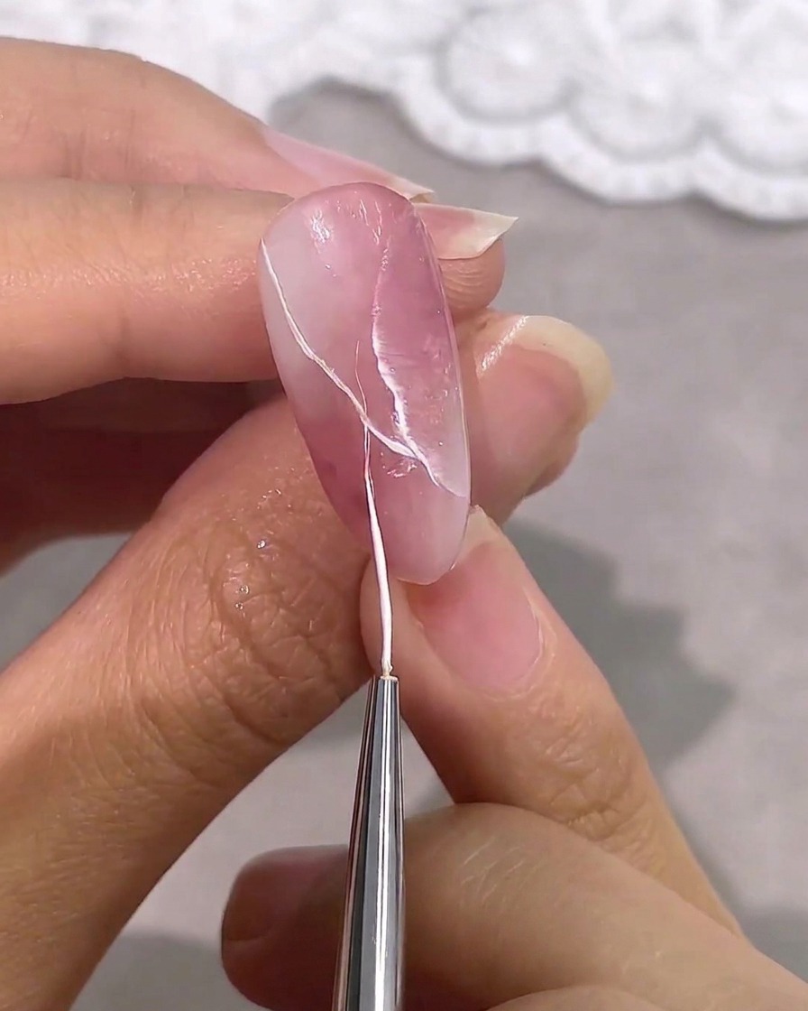 Ein feiner Liner-Pinsel fügt dünne, klare weiße Adern zu einem rosa-weißen Marmordesign hinzu.