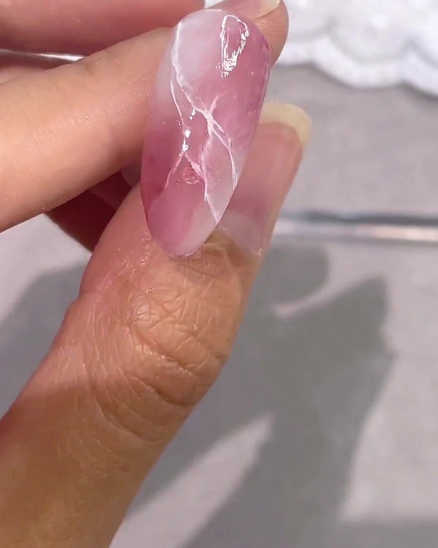 Ein fertiggestellter rosa Marmor-Gelnagel mit Silberakzenten und glänzendem Top Coat.