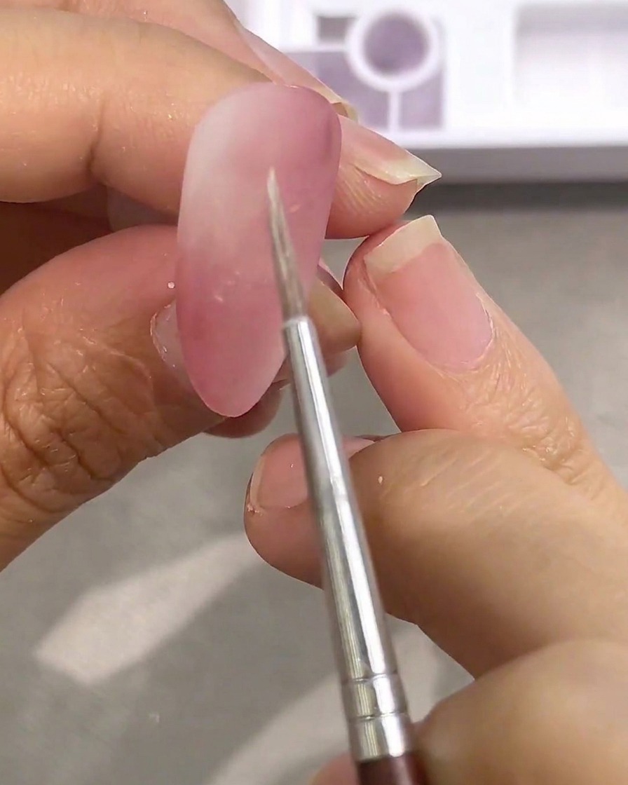 Nahaufnahme eines Detailpinsels, der in weiße Aquarellfarbe auf einer Palette getaucht wird.