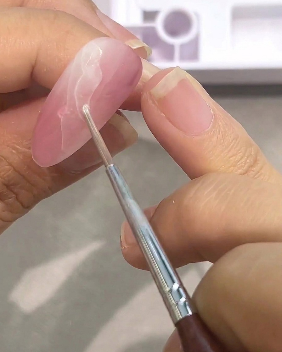 Nahaufnahme eines Pinsels, der eine zweite Schicht weiße Aquarellfarbe auf eine rosa Basis aufträgt.