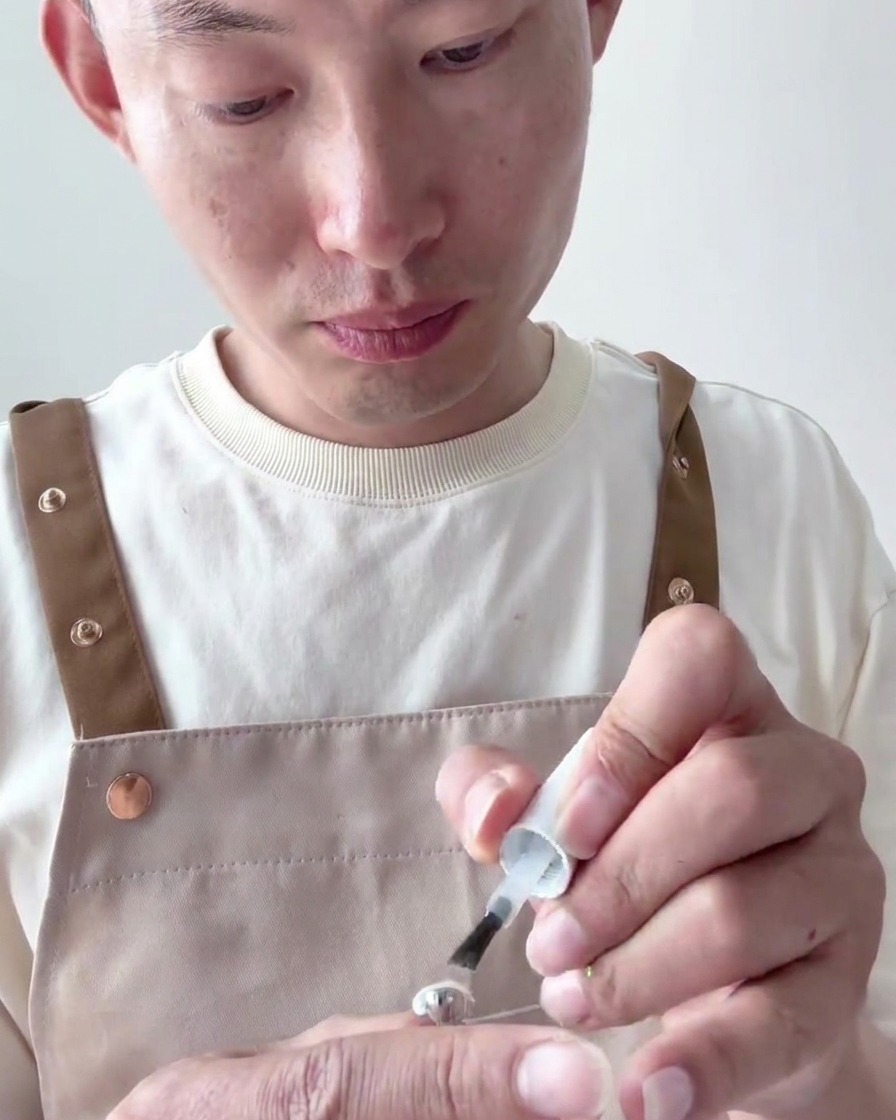 Nahaufnahme eines Pinsels, der eine zweite, deckende Schicht des milchig weißen UV-Lacks auf den Nageltip aufträgt.