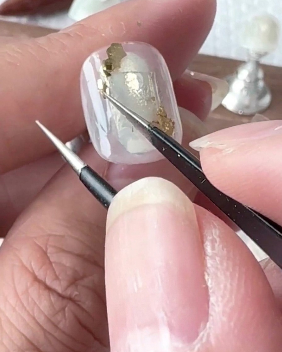 Ein kleiner Detailpinsel setzt winzige Tropfen von klarem Gel auf die Oberfläche des lackierten Nagels.