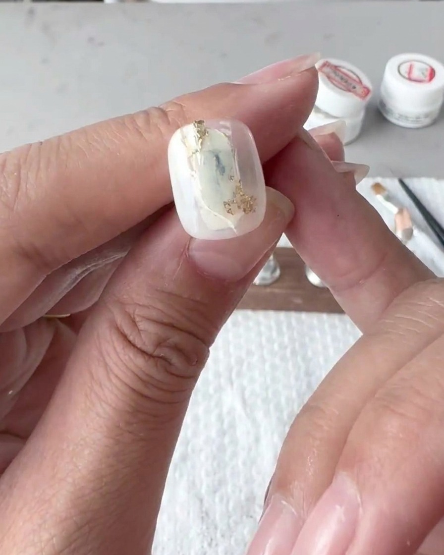 Nahaufnahme eines flachen Pinsels, der weiße Gel-Linien auf einem Nageltip zart verblendet und verwischt.