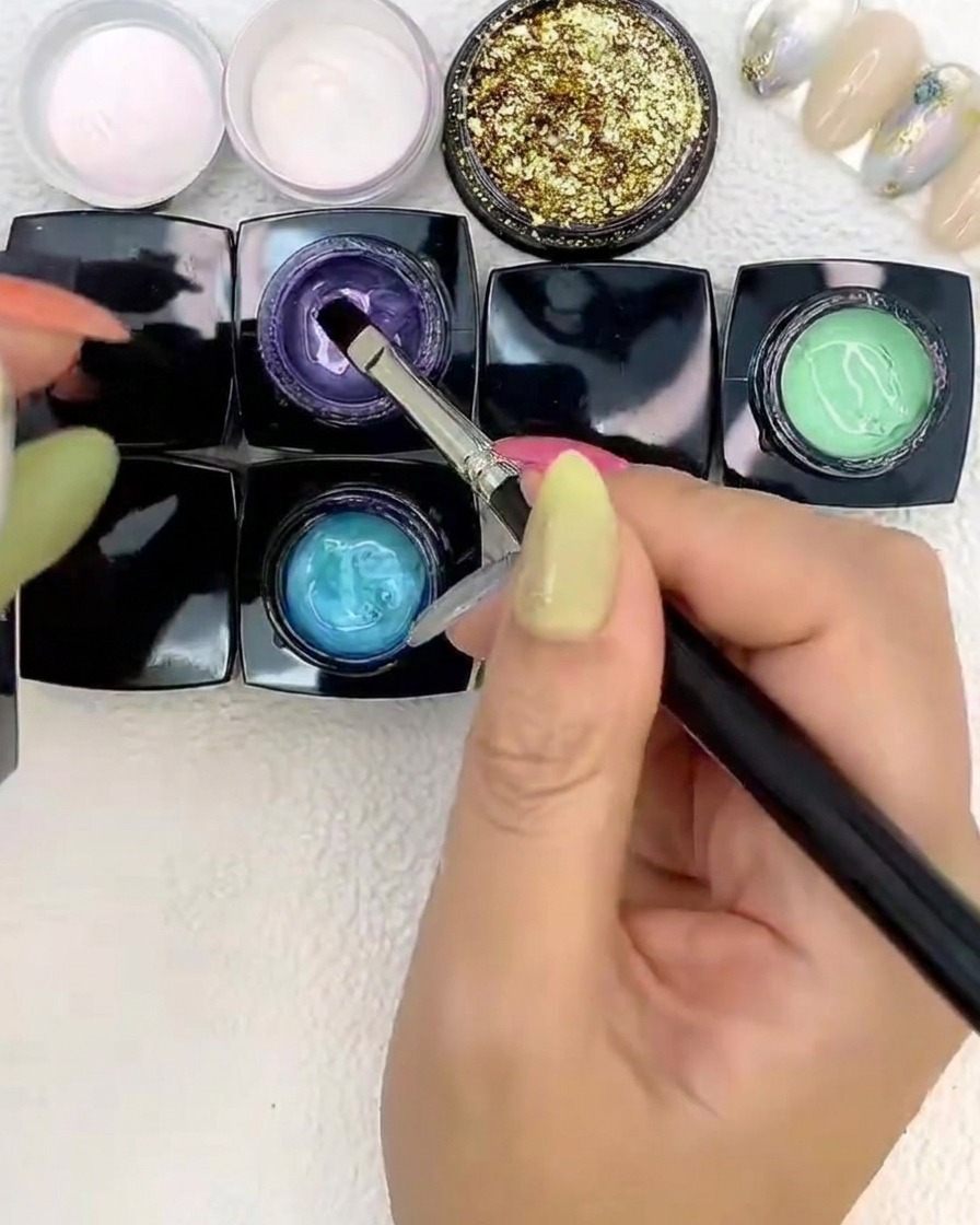 Ein Pinsel platziert violettes Gel neben Blau- und Grüntönen auf einem Nagel.