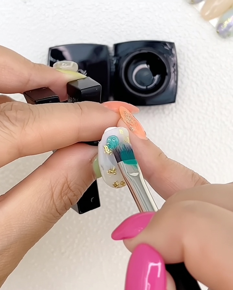 Nahaufnahme einer Hand mit mehrfarbig bemalten Gelnägeln unter einer professionellen UV-Lampe.