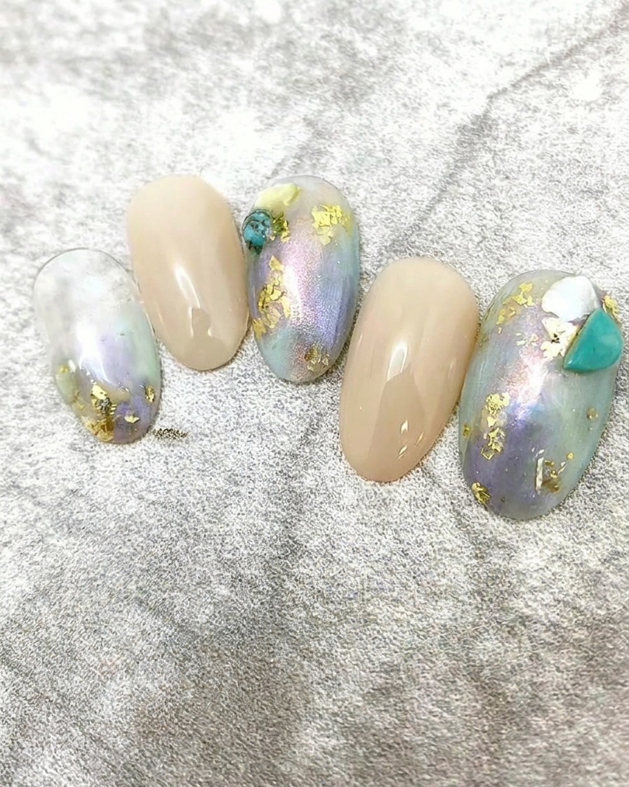 Winzige weiße Muschelflocken werden als dekorative Akzente auf ein Nageldesign aufgetragen.