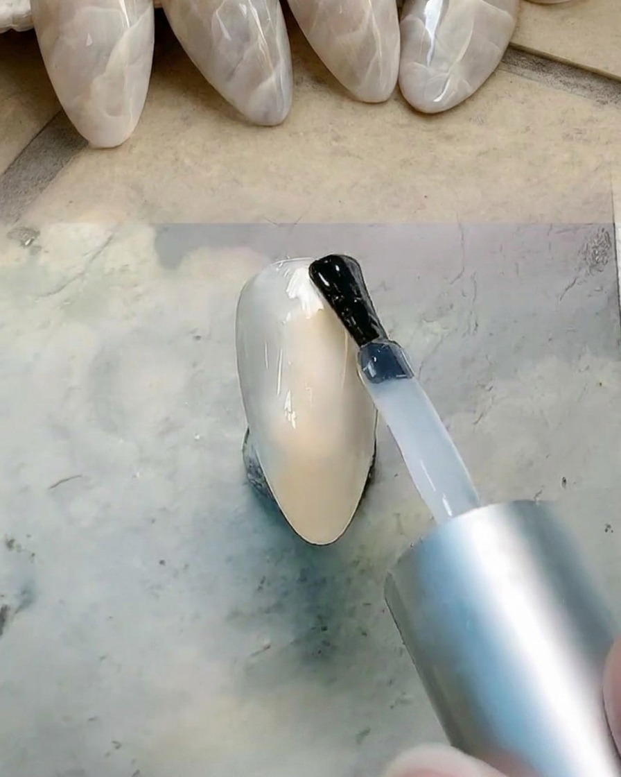 Ein Pinsel trägt klares Gel auf die Nageloberfläche auf, um das Verblenden vorzubereiten.