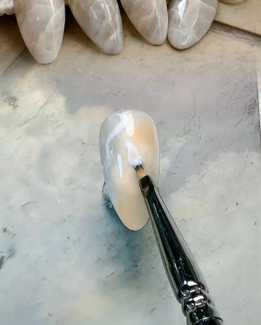 Ein flacher Pinsel verblendet braune und graue Gel-Farben auf dem Nagel zu einem weichen Übergang.