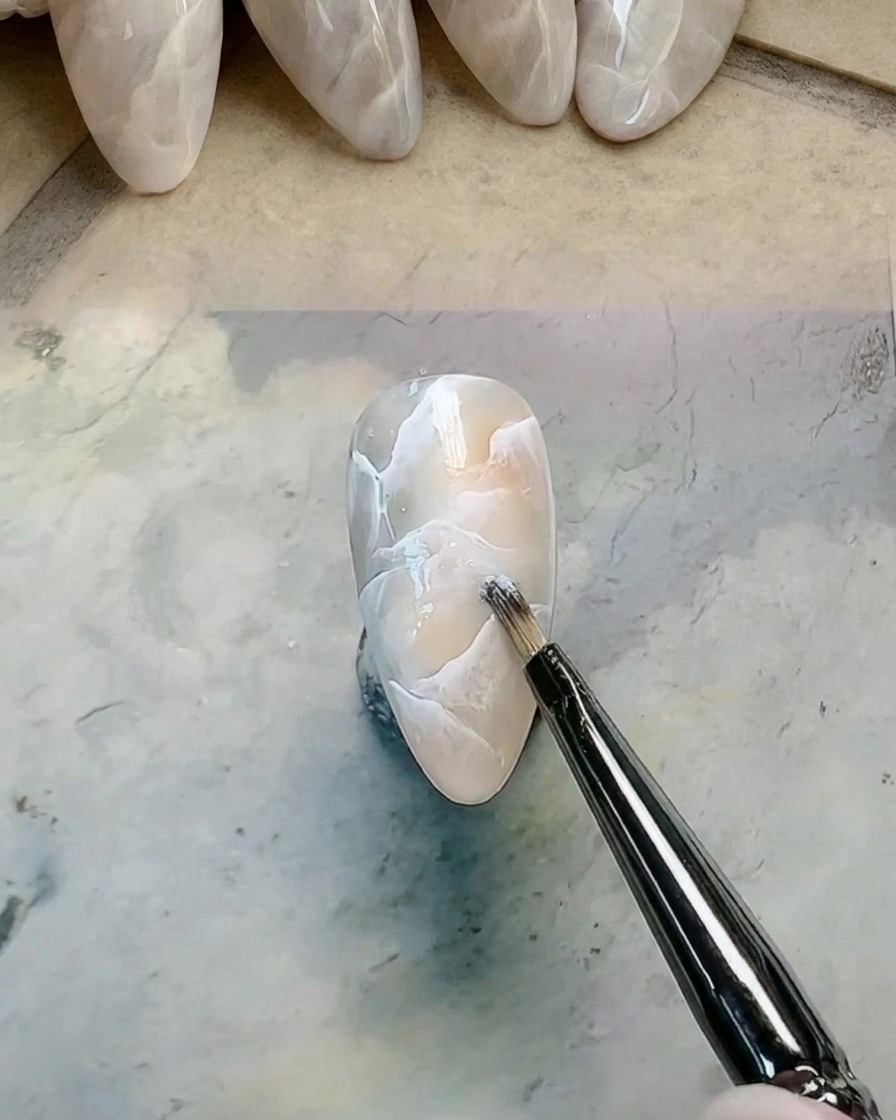 Ein Detailpinsel trägt zusätzliches weißes Gel auf das Marmor-Design auf und verwischt es.