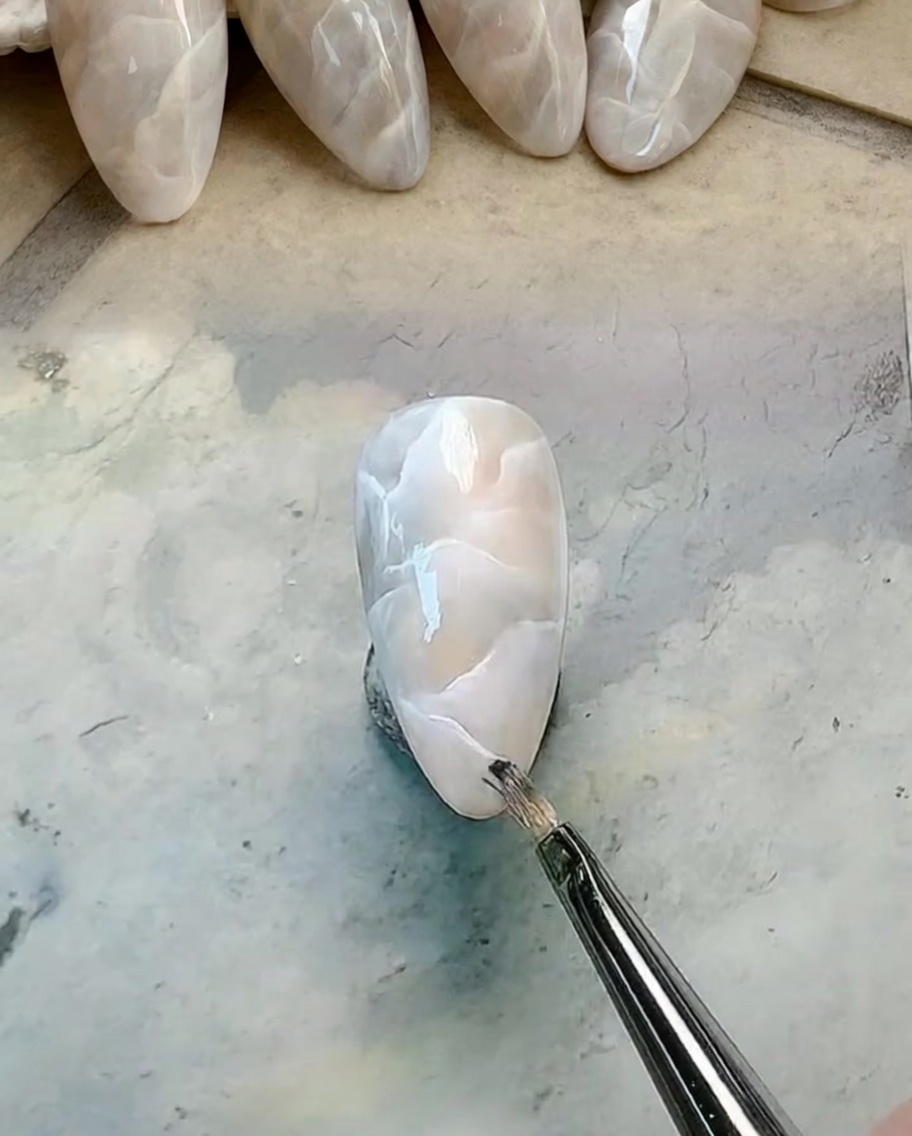 Ein feiner Liner-Pinsel zeichnet klare weiße Adern auf das milchig marmorierte Nageldesign.