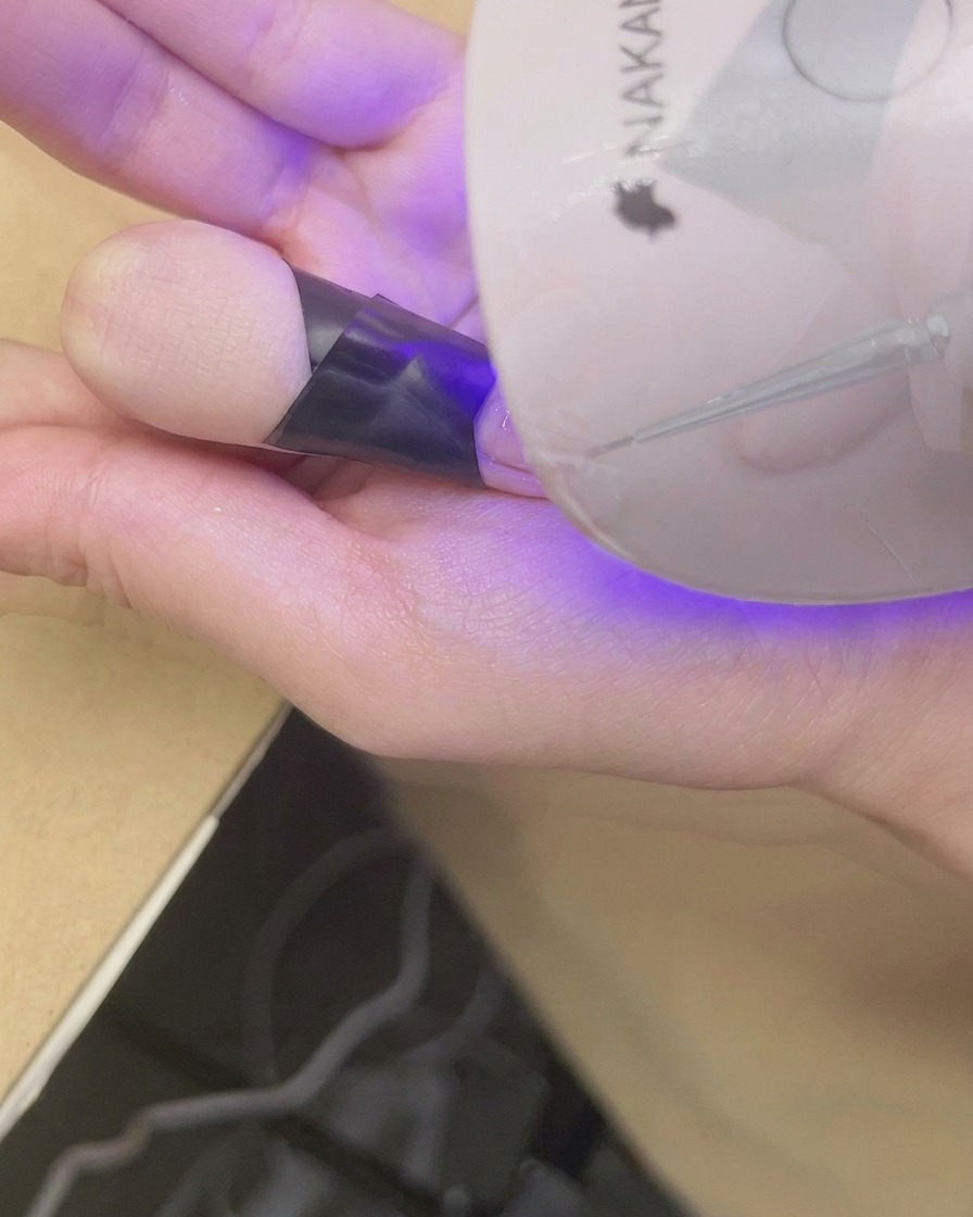 Ein Finger liegt unter einer kleinen UV/LED-Lampe zum Aushärten des Blush-Gradienten.