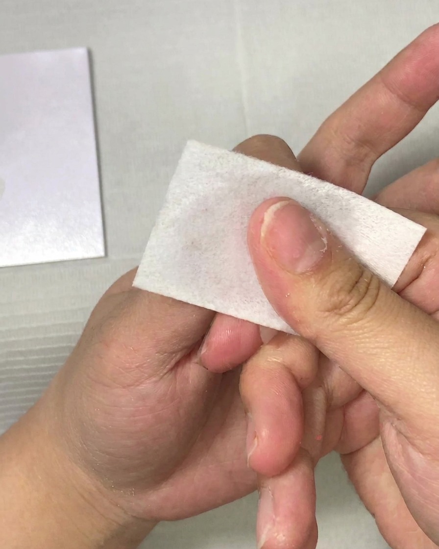 Eine Hand reinigt mit einer fusselfreien Zellette einen Fingernagel.