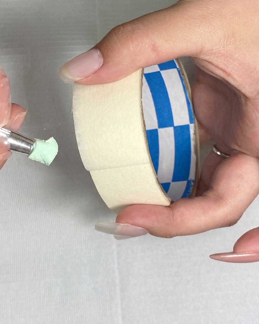 Ein Stück Klebeband wird verwendet, um feine Partikel von der Oberfläche eines grünen Schwamms zu entfernen.