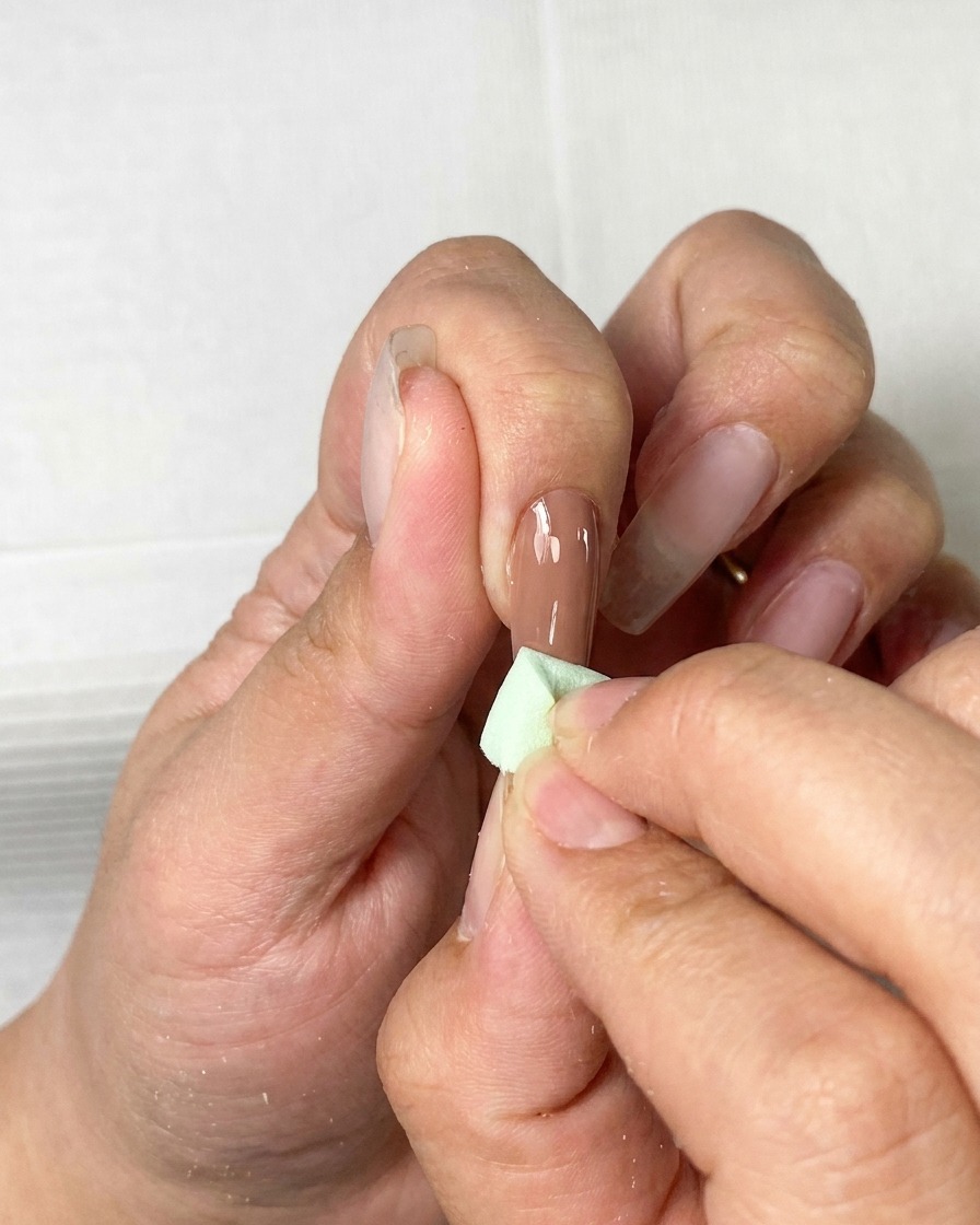 Ein Pinsel trägt eine gleichmäßige Schicht braunes Gel auf einen Naturnagel auf.