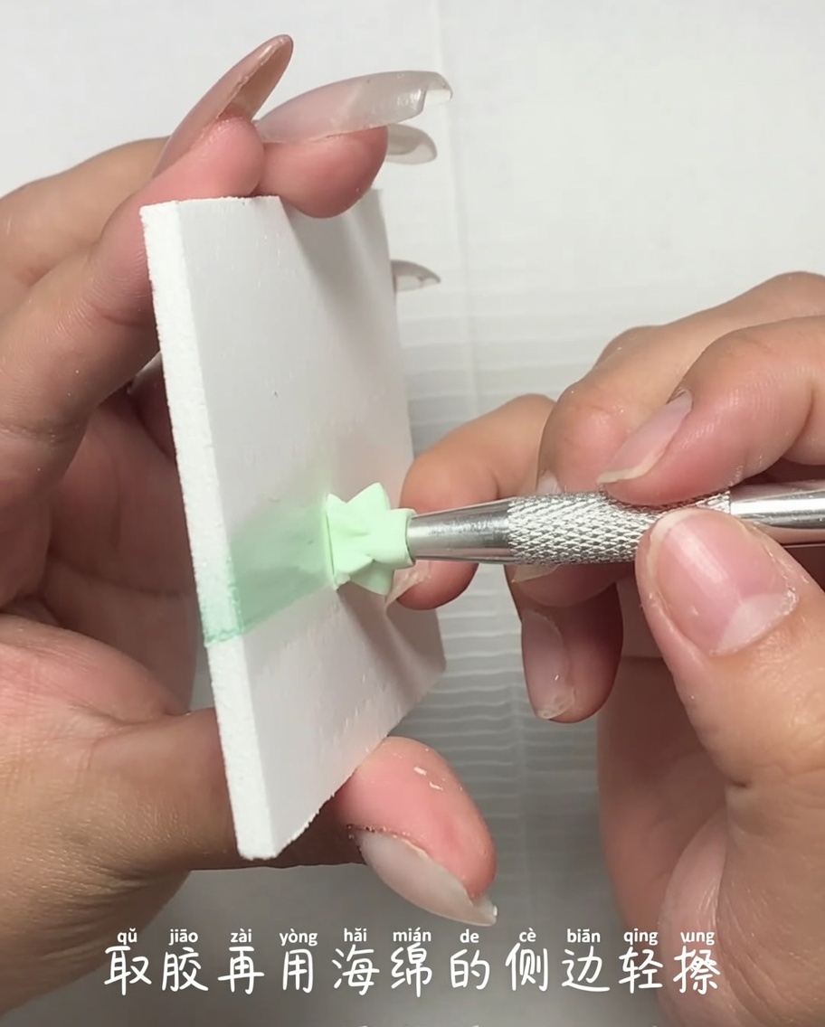 Ein Metallwerkzeug trägt eine kleine Menge hellgrünes Gel von einer Palette auf den Rand eines Make-up-Schwamms auf.