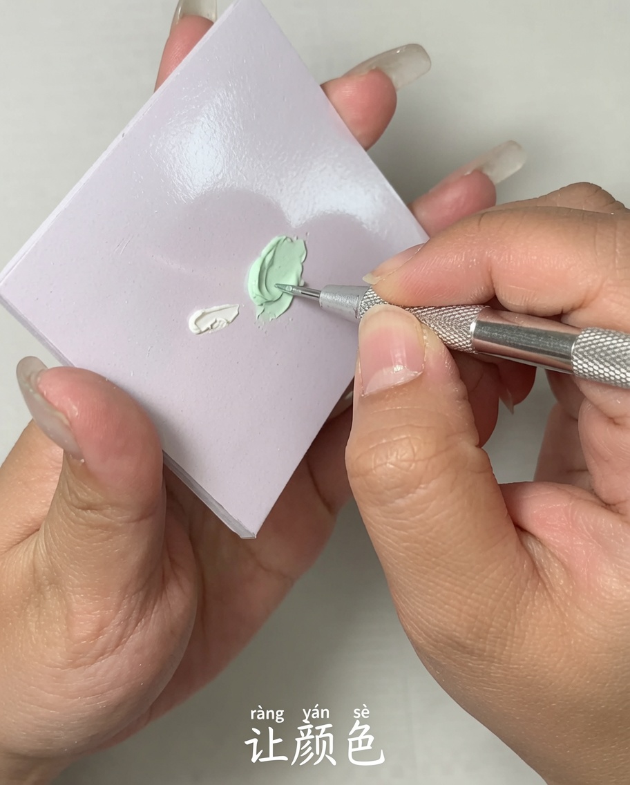 Ein Metallwerkzeug vermischt zwei verschiedene Gel-Farben auf einer flachen Palettenoberfläche.
