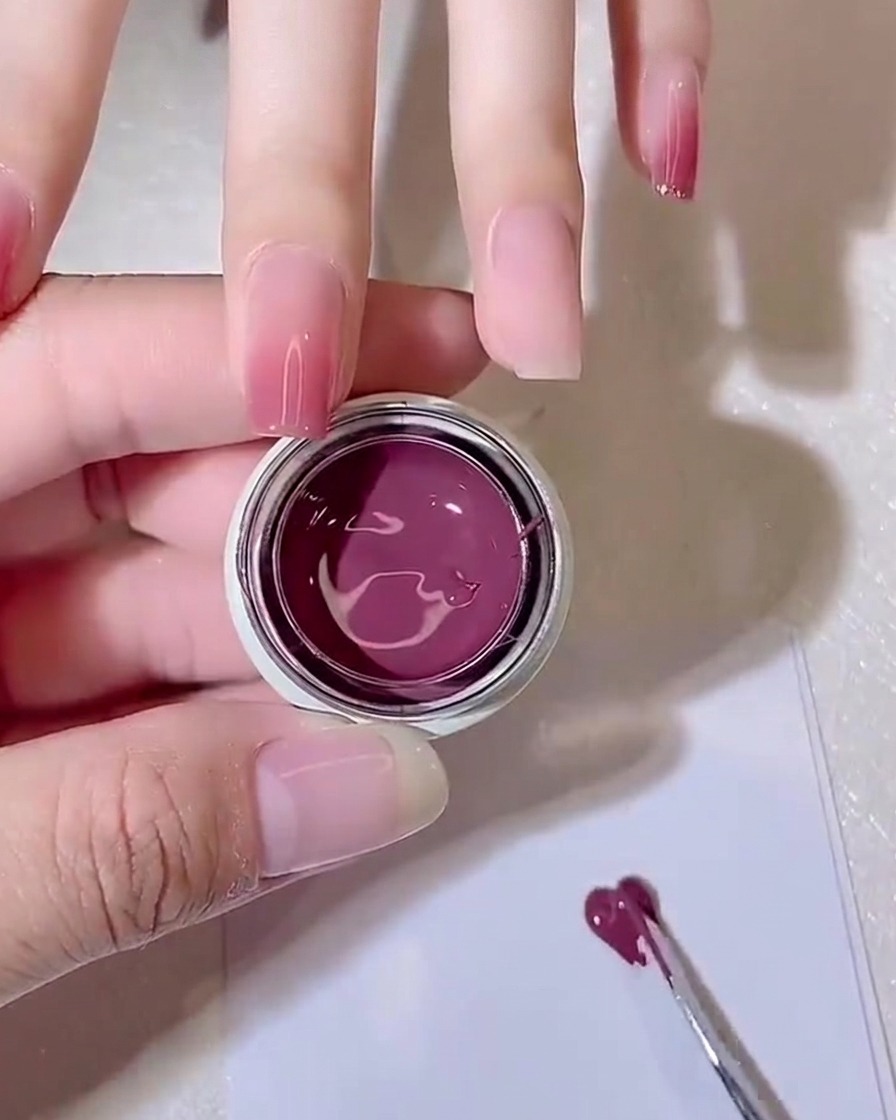 Ein Metallwerkzeug verteilt eine kleine Menge purpur-rosa Gel dünn auf einem Palettenpapier.