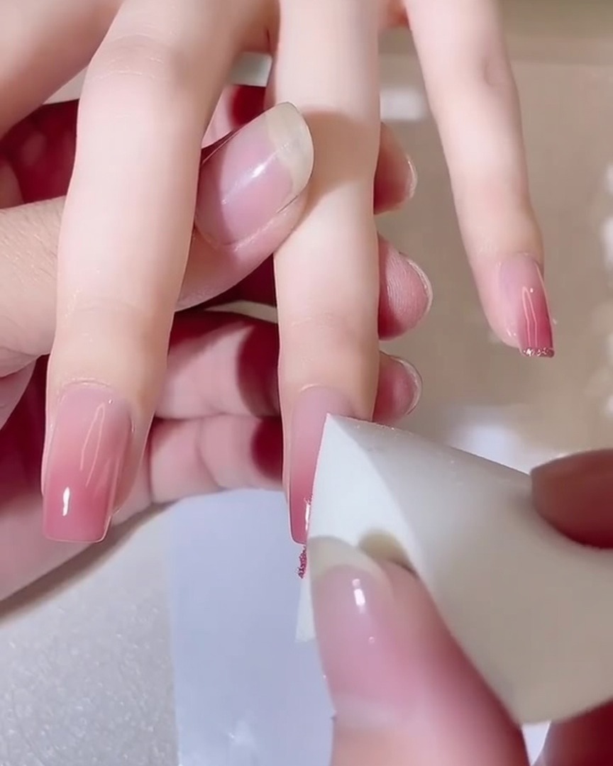 Nahaufnahme eines Schwamms, der auf einen Fingernagel tupft und einen tiefer werdenden rosa Gradient-Effekt zeigt.