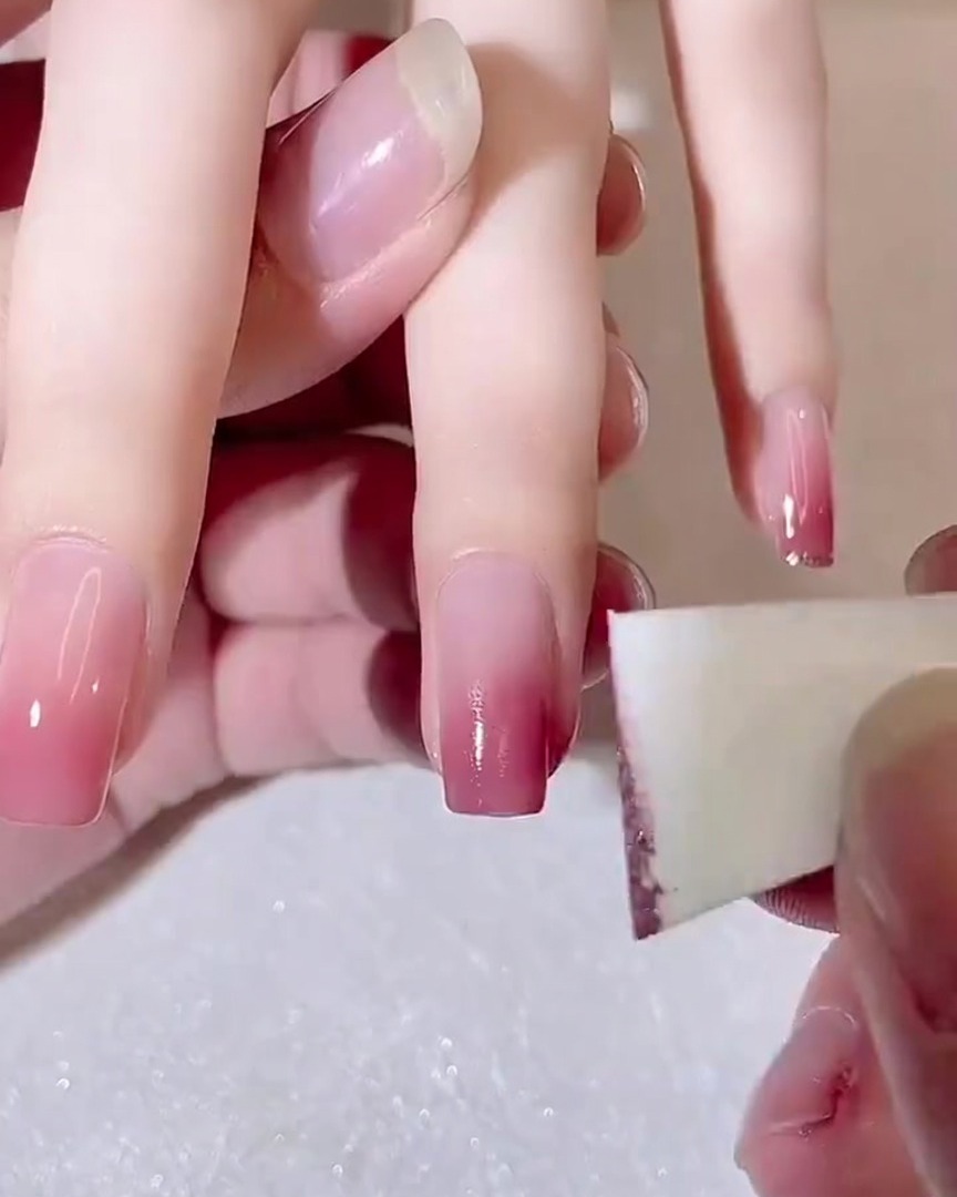 Nahaufnahme eines Make-up-Schwamms, der eine zweite Schicht dunkleres rosa Gel auf eine Nagelspitze tupft.