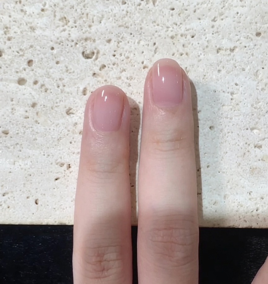 Ein Nagelpinsel, der sorgfältig die Kanten und die Spitze eines rosa lackierten Nagels nachbessert.