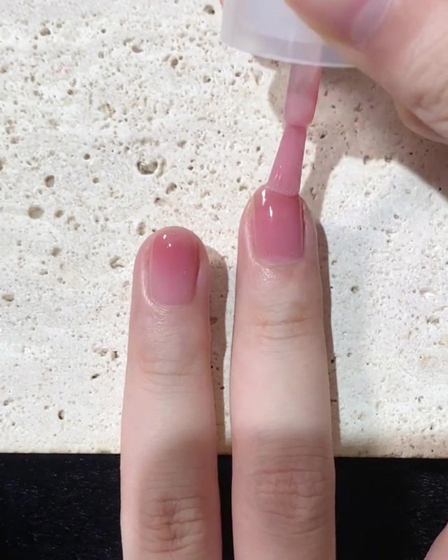 Ein Pinsel trägt eine letzte, konzentrierte Schicht rosa Lack gezielt auf die Nagelspitze auf.
