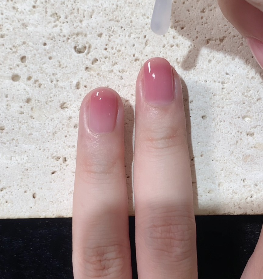 Ein Pinsel trägt einen klaren Glanz-Überlack über den fertigen Ombré-Nagel auf.