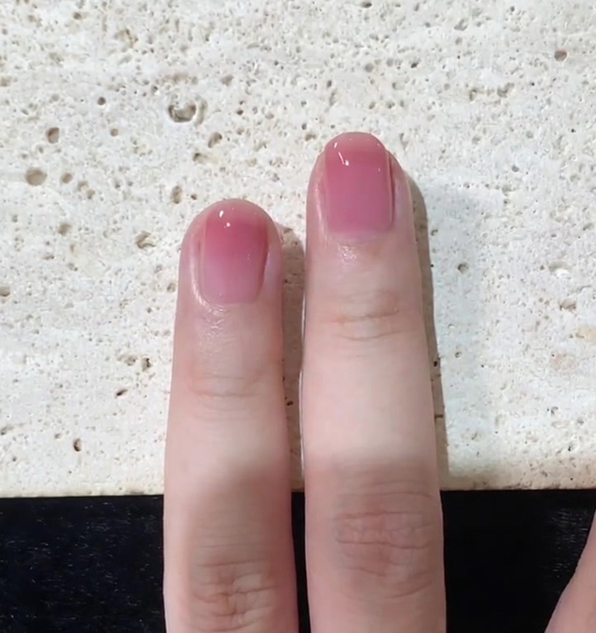 Nahaufnahme einer letzten Top-Coat-Schicht, die auf einem rosa Ombré-Nagel geglättet wird.